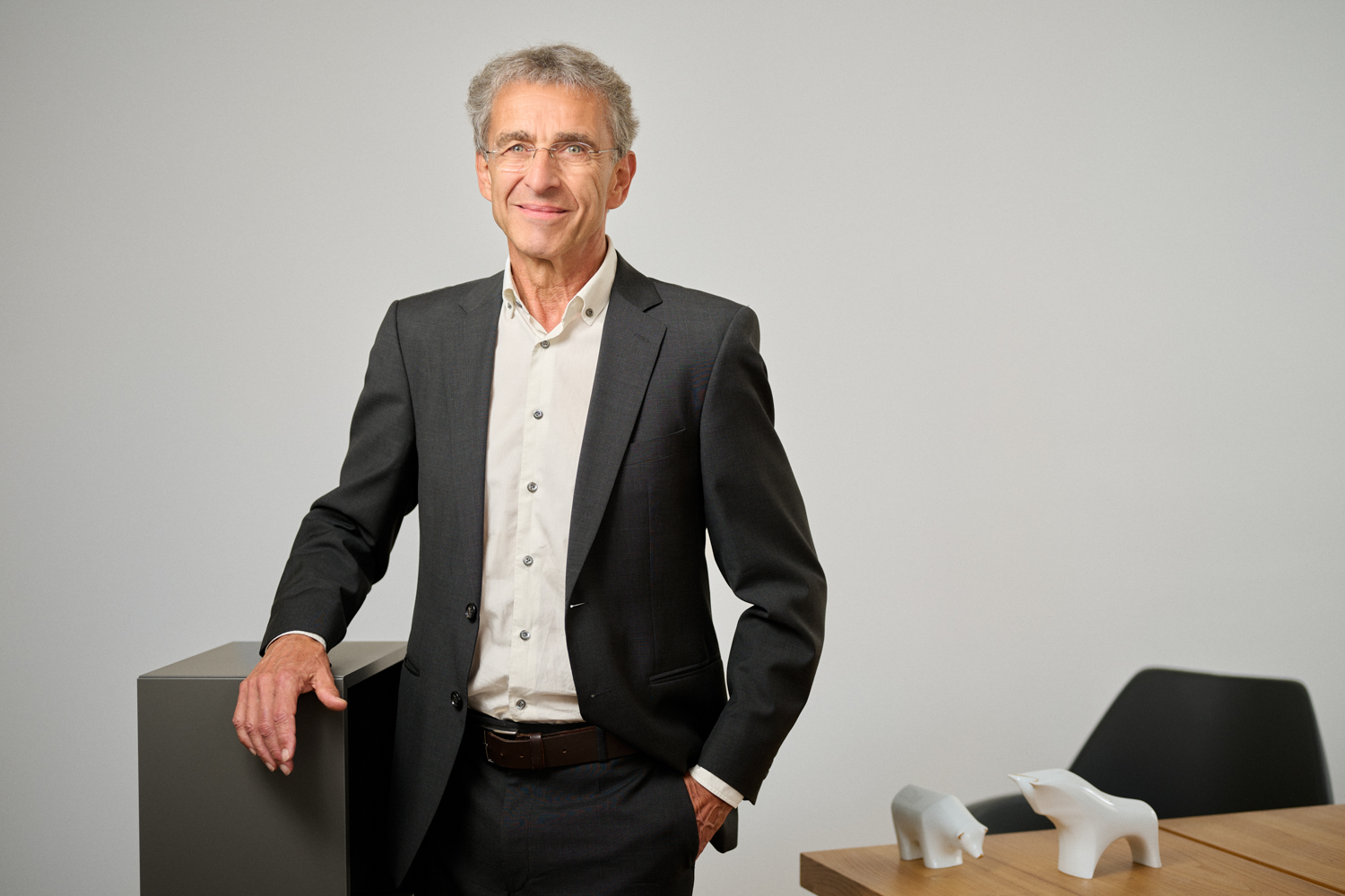Portrait von Eberhard Niedermaier: Ein älterer Mann mit hellgrauen Haar und Brille, in dunkelgrauen Anzug und weißem Hemd steht lächelnd in einem modernen Büro. Eine Hand ruht auf einem dunklen Möbelstück, im Hintergrund ein Tisch mit weißen Stier- und Bärfiguren.